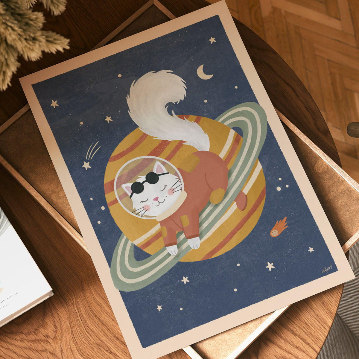Illustrated poster of a white cat in a rust spacesuit lying on a golden ringed planet in a navy sky