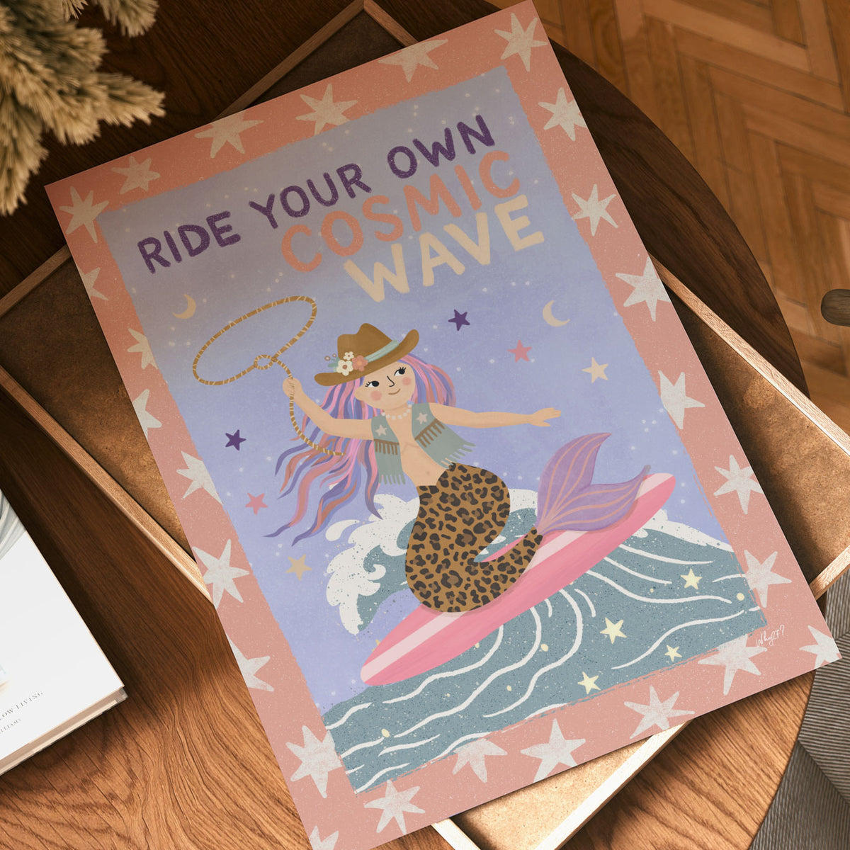 Illustrated poster of a cowgirl mermaid surfing a wave with a lasso under the words ride your own cosmic wave