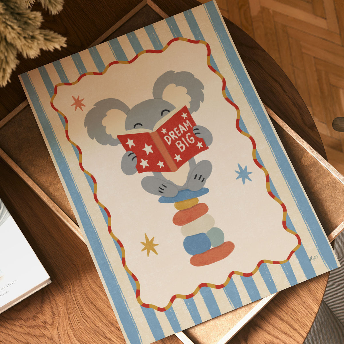 Illustrated poster of a koala on stacked stones reading a red book that says dream big
