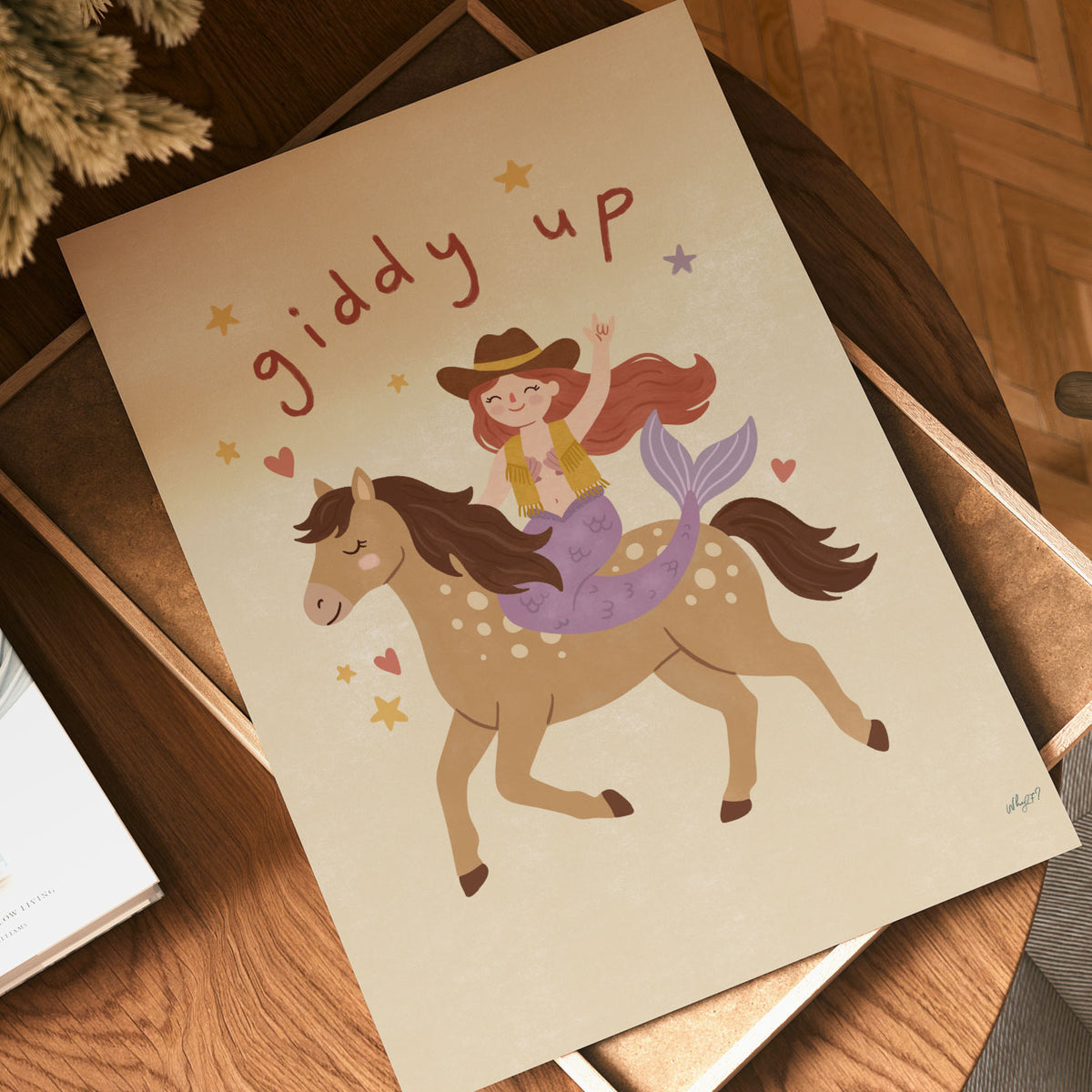 Illustrated mermaid in a cowboy hat and fringed vest riding a spotted horse, with hand-lettered giddy up above, on a cream background.