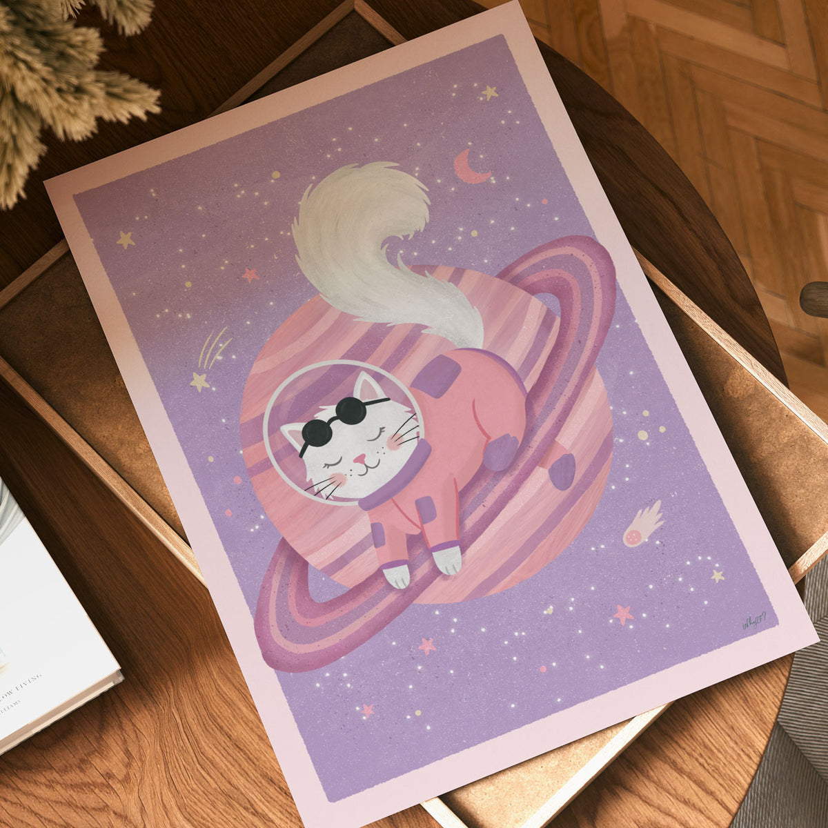Illustrated poster of a white cat in a coral spacesuit resting on a pink ringed planet in a lilac sky