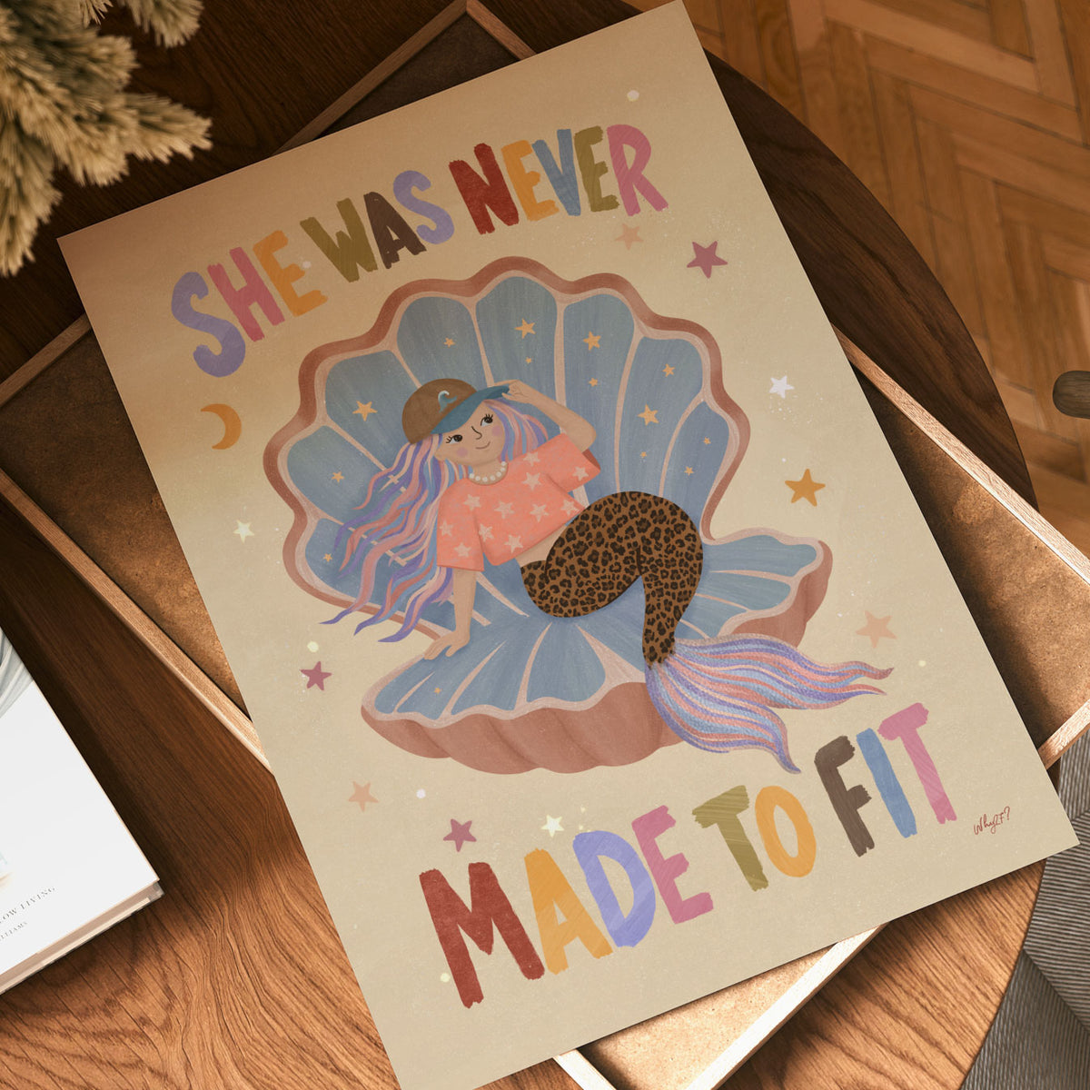 Illustrated poster of a mermaid in a shell wearing a cap with the words she was never made to fit