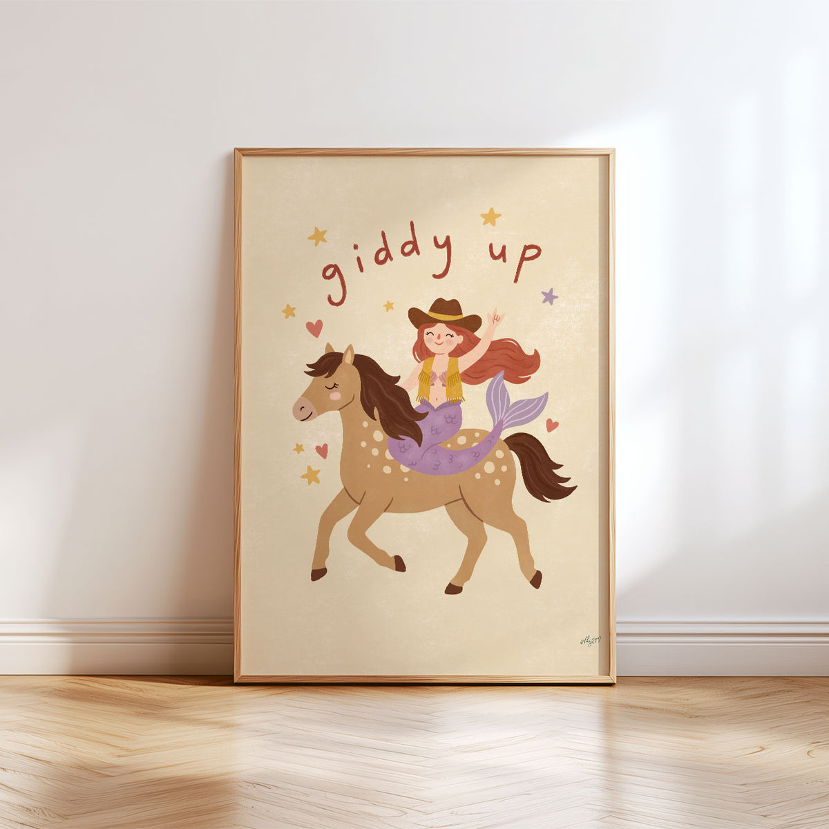 Illustrated mermaid in a cowboy hat and fringed vest riding a spotted horse, with hand-lettered giddy up above, on a cream background.